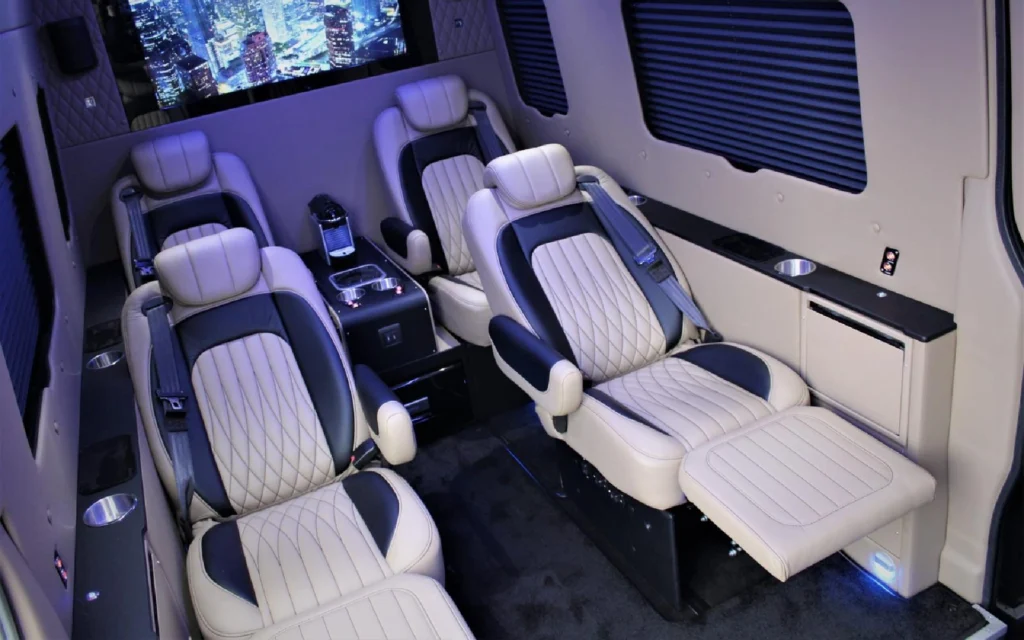 Luxurious reclining seats with beige quilted leather upholstery inside the Mercedes Jet Class Sprinter, featuring cupholders, ambient lighting, and a high-definition screen.