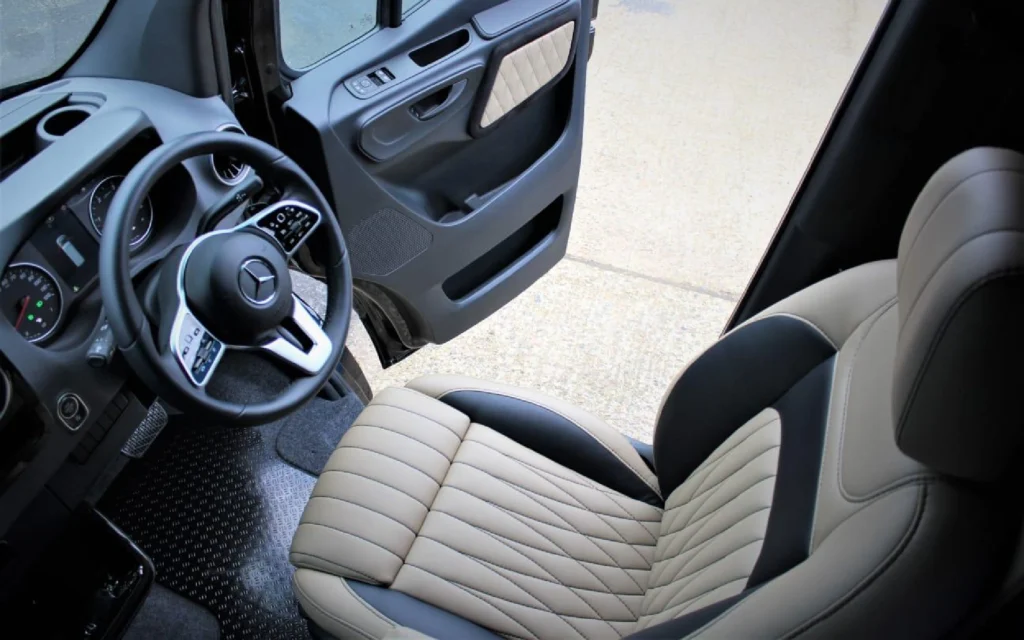 Luxurious driver's cabin of the Mercedes Jet Class Sprinter featuring a beige quilted leather seat, a modern steering wheel, and detailed dashboard controls.