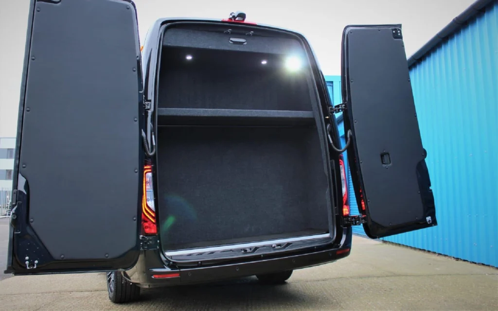 Open rear luggage compartment of the Mercedes Jet Class Sprinter, featuring ample storage space with a partition shelf and carpeted interior.