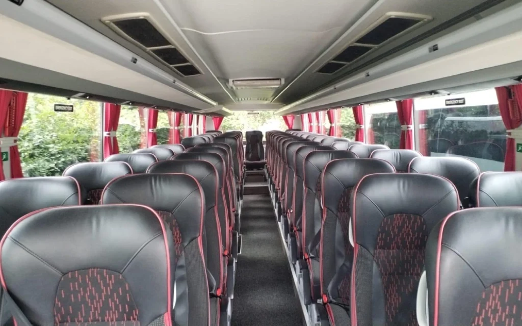 Spacious and modern interior of the YUTONG T122HDH coach, featuring rows of black leather seats with red accents, wide aisles, and large windows with red curtains.